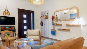 A living room with a brown leather sofa, a white armchair, a round coffee table, a television, and a door with a mirror and hats on the wall. - El Jardin de Lara, Casa con Parking Son Españolet-palma (Palma de Mallorca)