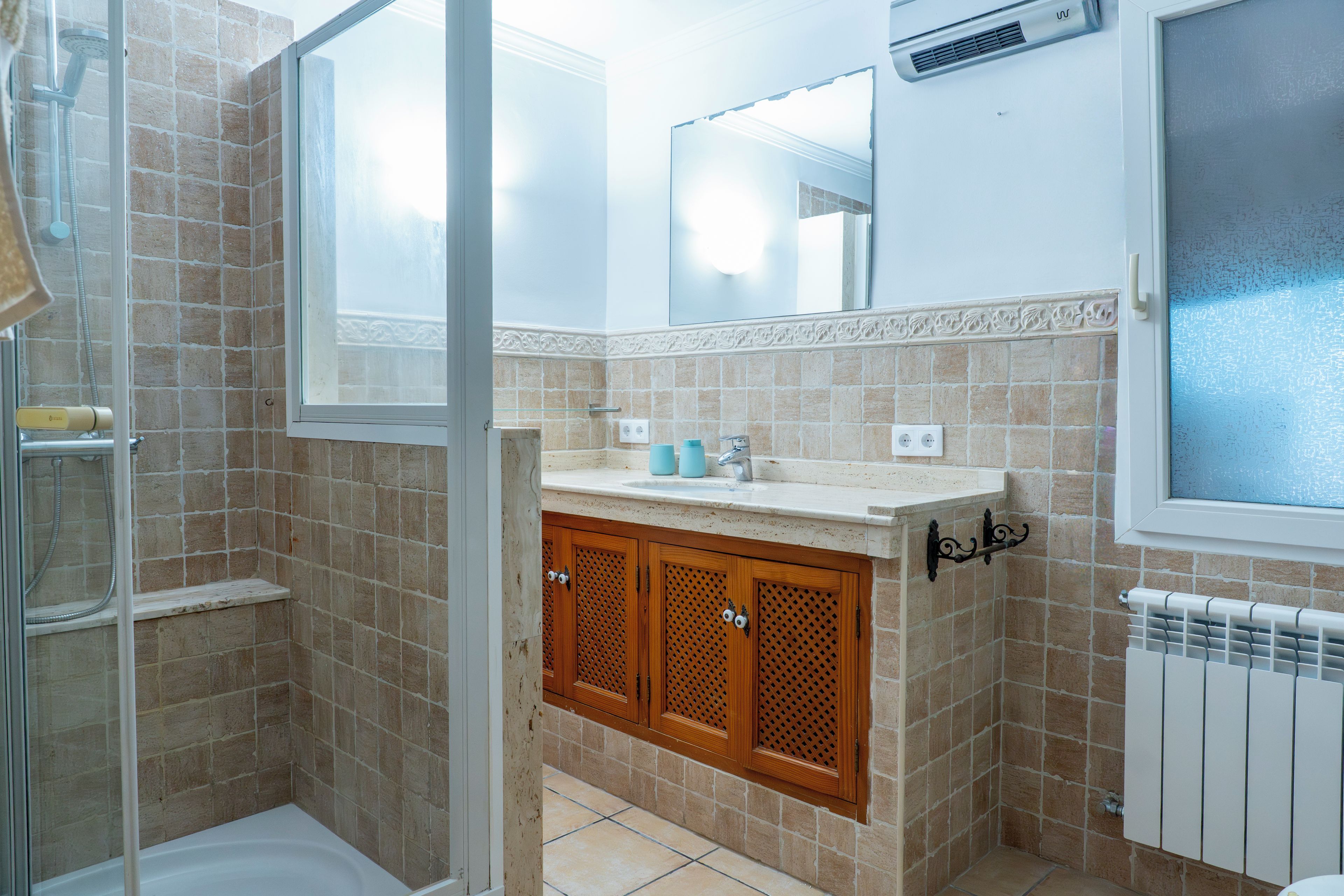 A bathroom with a shower, a sink with a mirror above, and a radiator.