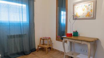 A room with a window, a mirror, a wooden desk, and a small stool.