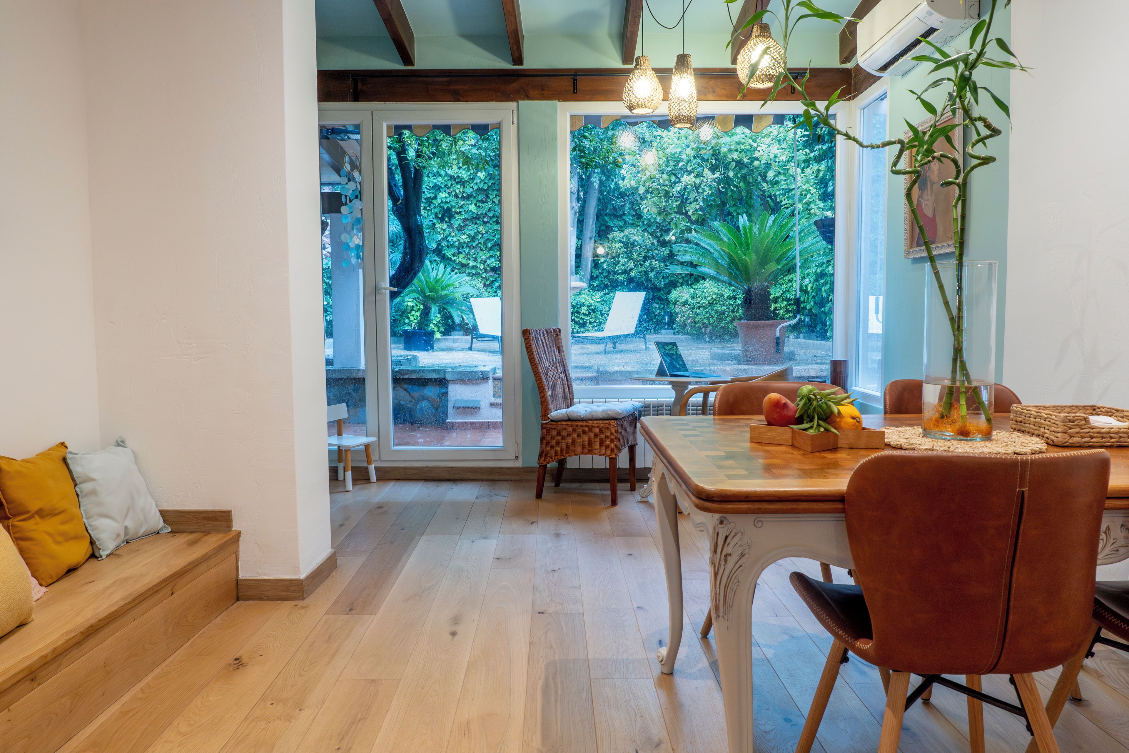 Un comedor con una mesa de madera, sillas y vistas a un jardín a través de puertas de cristal.