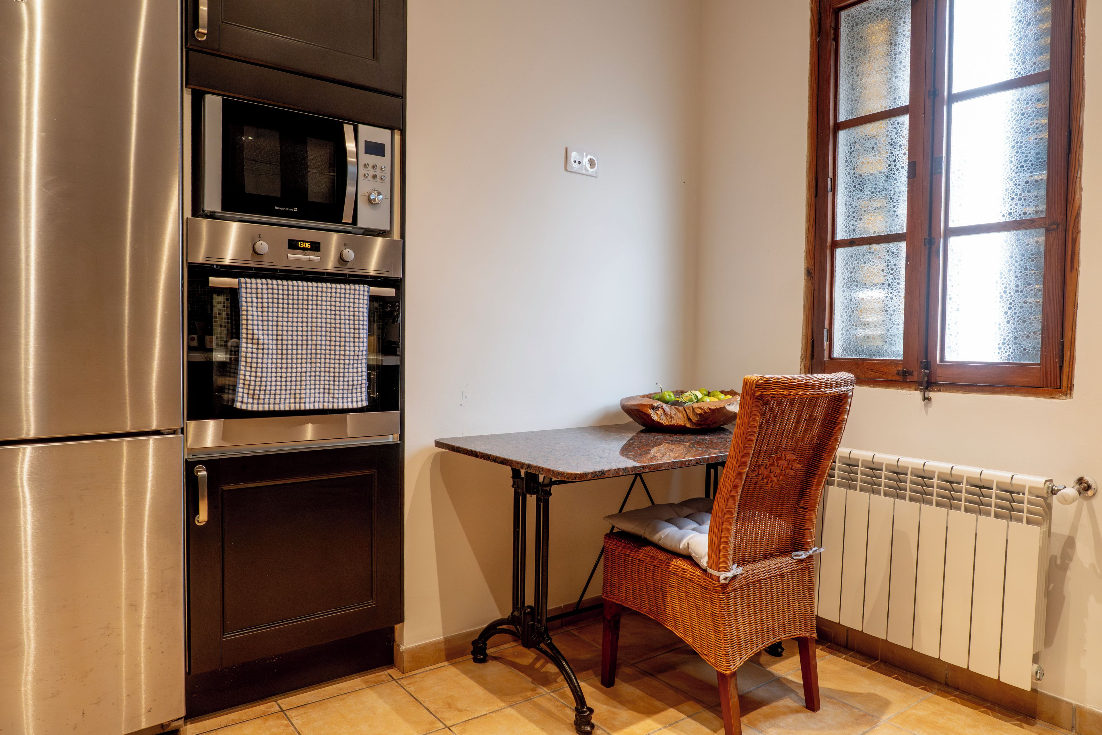 A kitchen with stainless steel appliances, a checkered towel, a wicker chair, and a window with frosted glass.