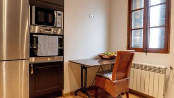 A kitchen with stainless steel appliances, a checkered towel, a wicker chair, and a window with frosted glass.
