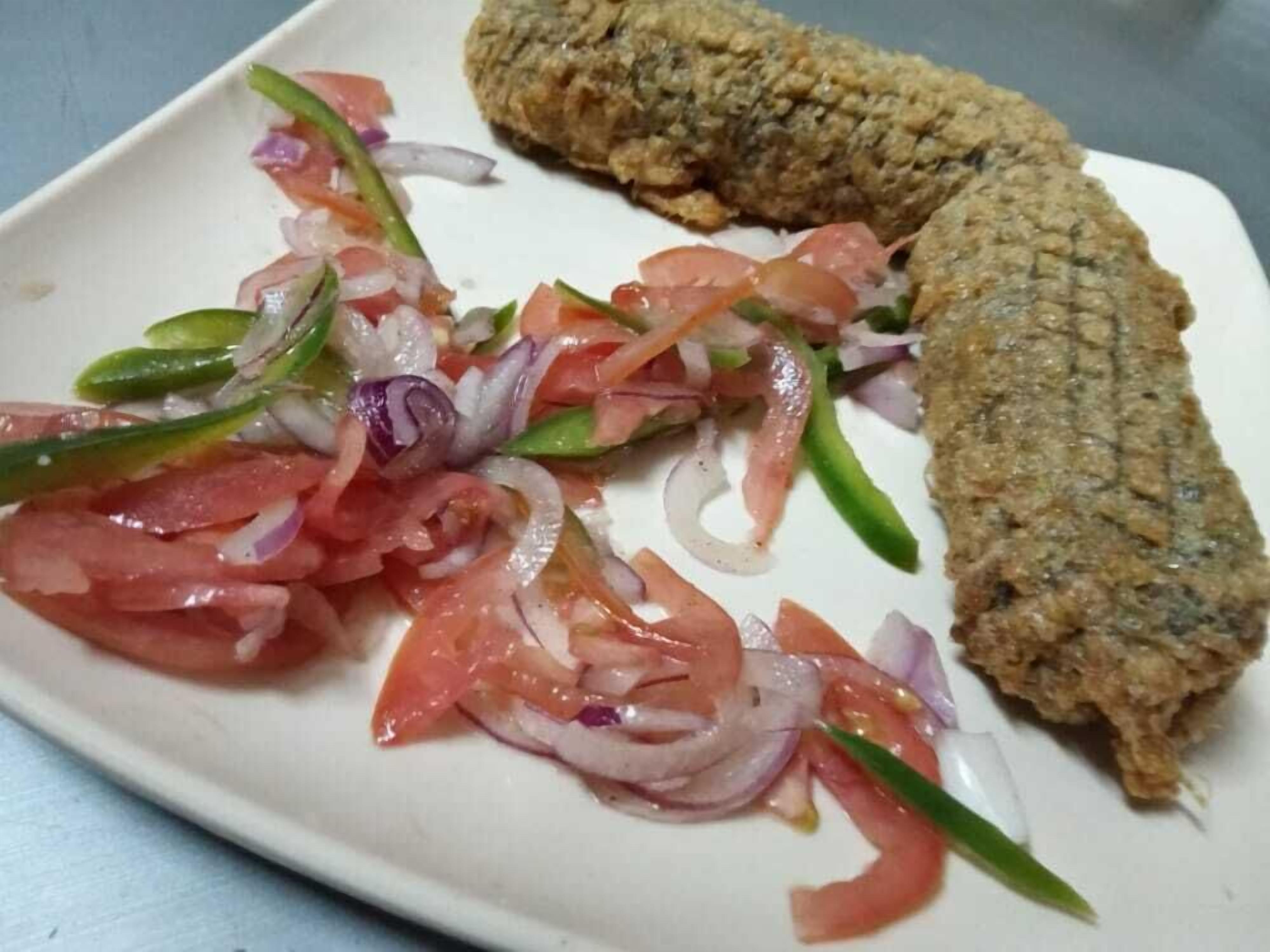 A plate with a breaded fish fillet and a side salad of tomatoes, onions, and green peppers.