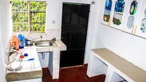 Une petite cuisine avec un évier, une fenêtre munie d’une grille métallique et une étagère contenant diverses bouteilles.