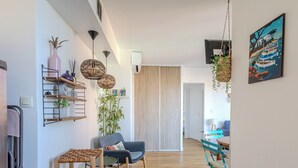 A modern living room with a blue sofa, wooden coffee table, and a dining area with a blue chair and table. There are shelves with decorative items and a large bamboo plant. - (014) Port Vauban et piscine (Antibes)