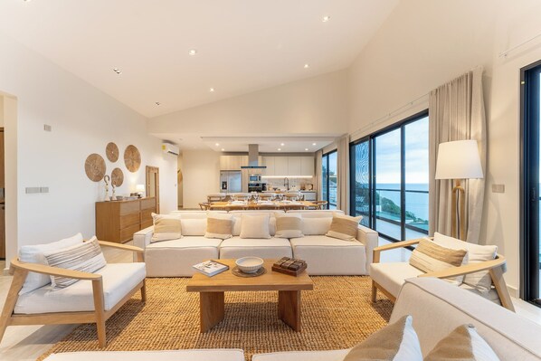 A modern living room with a sofa set, a coffee table, and a view of the kitchen and dining area. - Stunning Oceanview Penthouse at Paradise Cove (Huatulco)