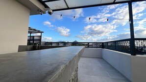 Una terraza en la azotea con un bar de concreto, techo metálico y vistas al cielo.