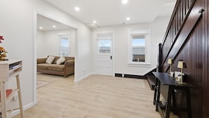 A spacious living area with a wooden floor, a brown sofa, a white door, and a staircase with dark wood railings. - Heishman Historic Hillside Home 4 Bedroom Home (Wardensville)