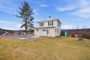 A two-story house with a front porch, a garage, and a large tree in the yard. - Heishman Historic Hillside Home 4 Bedroom Home (Wardensville)