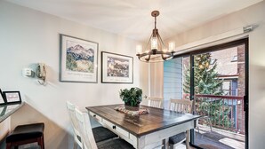 Un coin repas avec une table en bois, des chaises blanches, un lustre et des tableaux encadrés accrochés au mur.