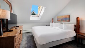 Une chambre d’hôtel avec un grand lit, un téléviseur posé sur une commode en bois, un tableau accroché au mur et une fenêtre donnant sur un immeuble.