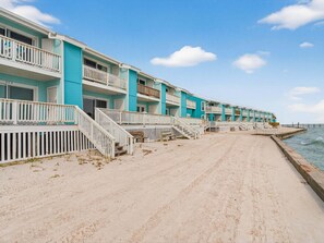 A row of beachfront hotel buildings with balconies and a sandy walkway leading to the water. - Bayfront Kontiki 301 3 Bedroom Condo (Rockport)