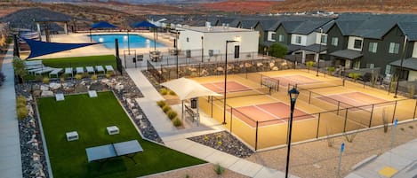 A residential area with a swimming pool, tennis courts, and houses with dark roofs.