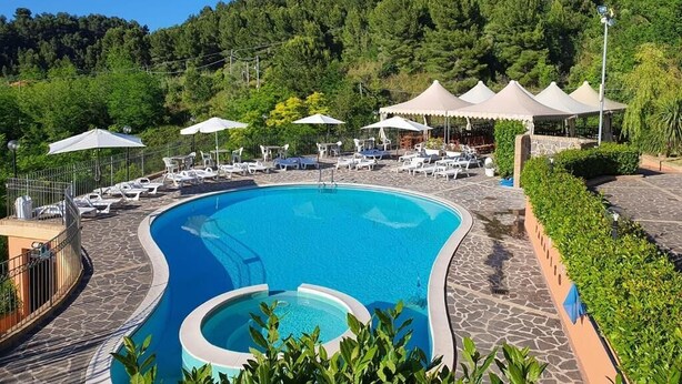 A swimming pool with lounge chairs and umbrellas, surrounded by greenery and a hilly landscape. - Paradiso Country house (Pescara)