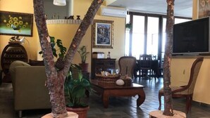 A living room with a sofa, coffee table, and chairs. There are potted plants and a painting on the wall. - Paradiso Country house (Pescara)