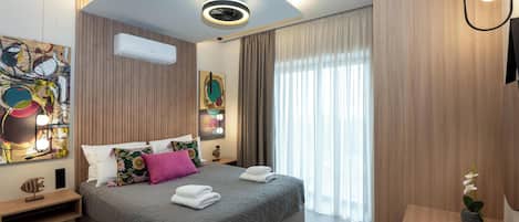 A modern hotel room with a large bed, a bedside table, an air conditioning unit, and a window with curtains.