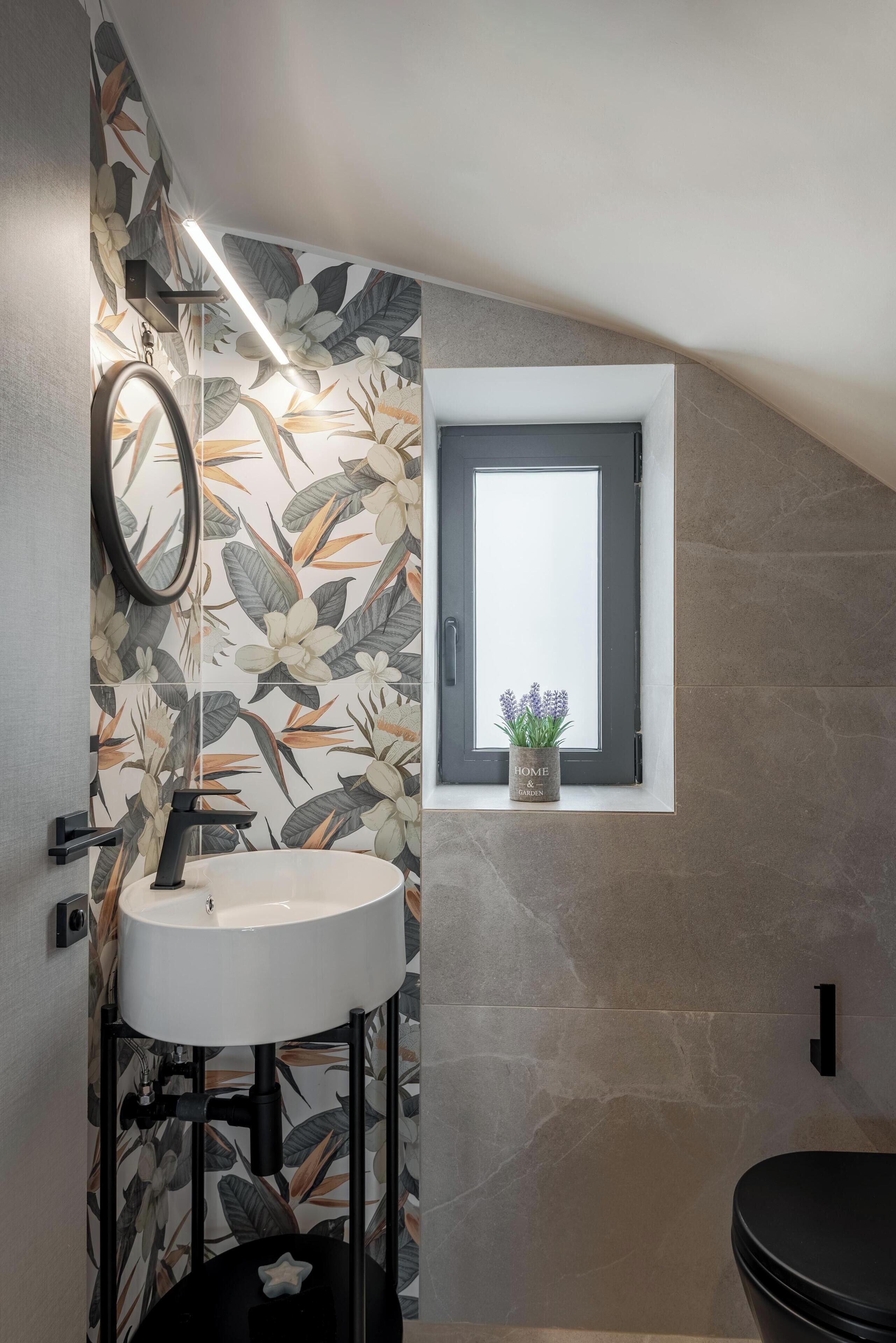 Ein Badezimmer mit einem runden Waschbecken, einem Spiegel und einem Fenster mit einem Blumentopf.