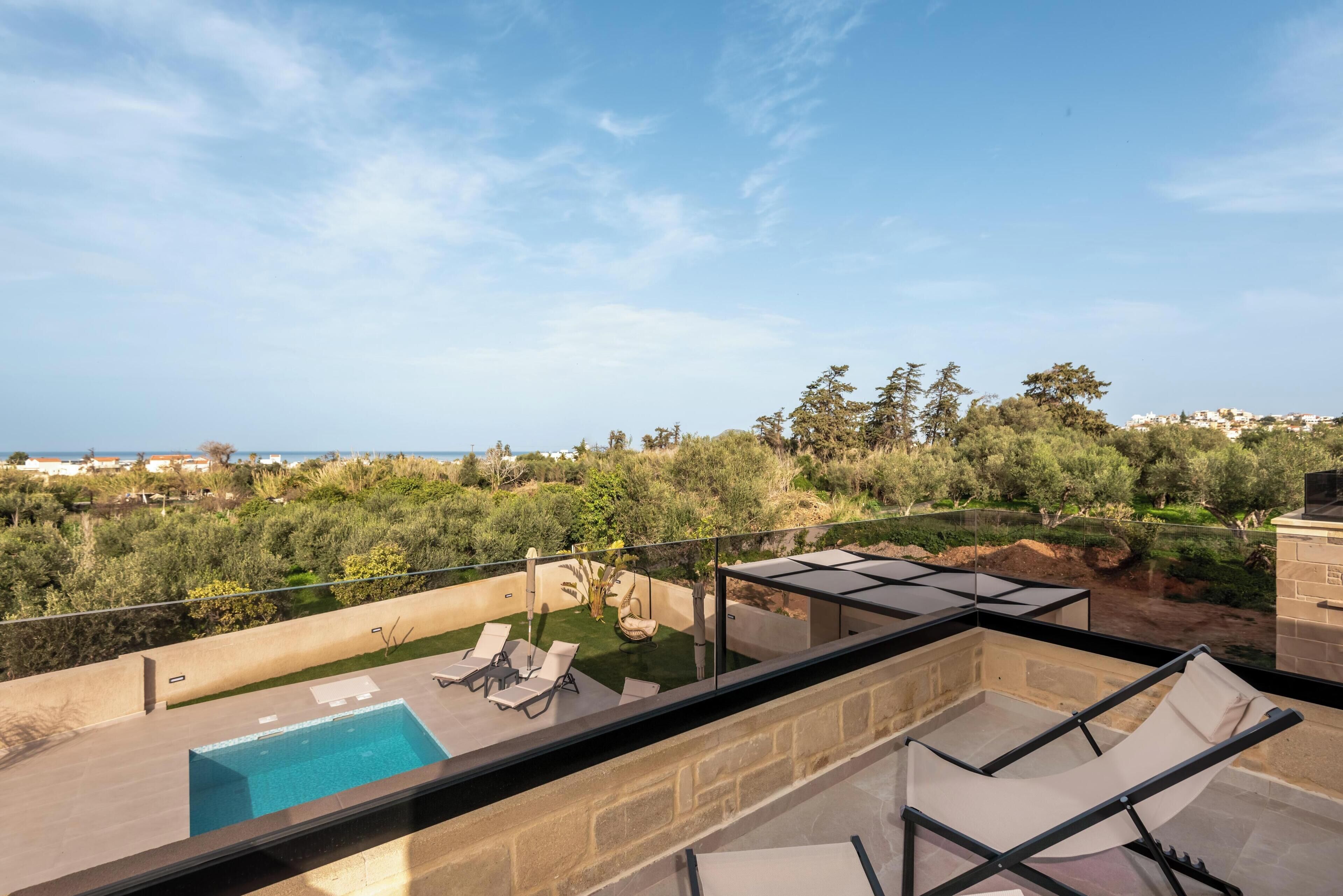 Eine Dachterrasse mit Swimmingpool, Liegestühlen und Blick auf das Meer und die grüne Umgebung.