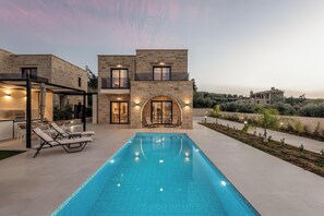A modern house with a swimming pool, outdoor seating, and a view of the surrounding landscape. - Golden Silence (Platanias)