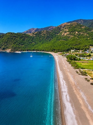A coastal landscape with a clear blue sea, a sandy beach, and a mountainous backdrop. - Emir Palas Hotel (Koycegiz)