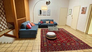 Ein gemütliches Wohnzimmer mit einem blauen Ecksofa, einem gemusterten Teppich und einer Holzbalkendecke.