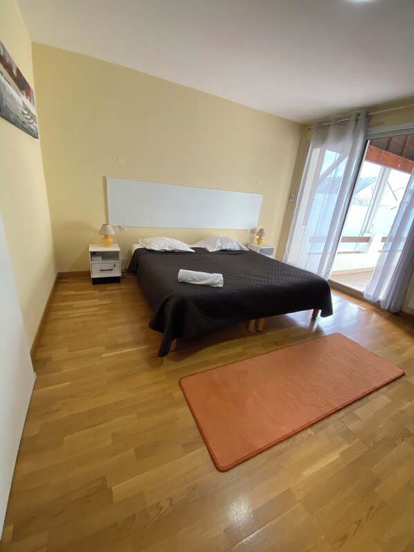 A bedroom with a bed, nightstands, a window, and a wooden floor.