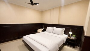 A neatly arranged bedroom with a large bed, a nightstand, a chair, and a ceiling fan. - Landmark Inn (Lanka)