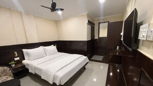 A hotel room with a bed, a nightstand, a chair, a TV, and a wardrobe. - Landmark Inn (Lanka)
