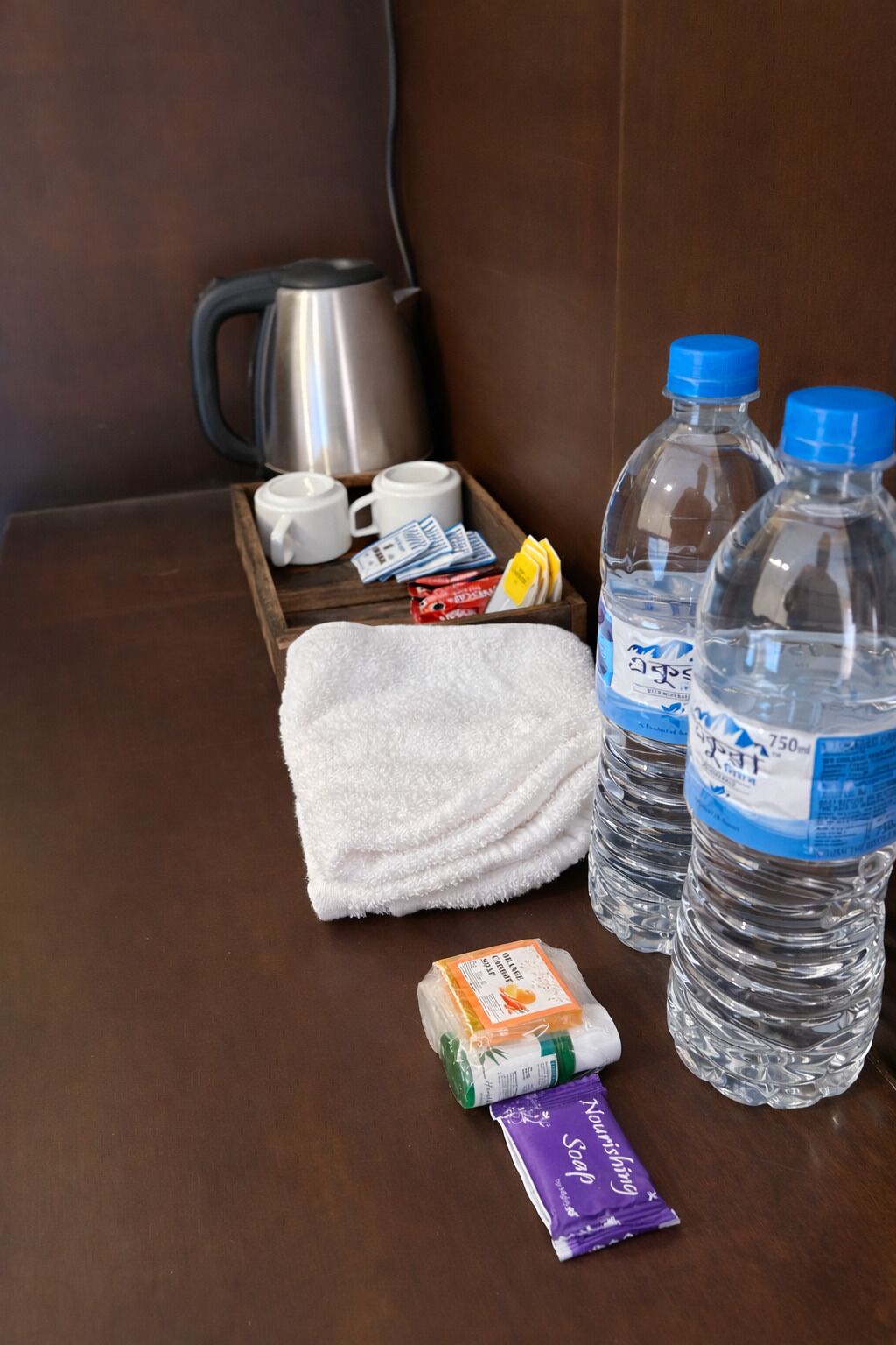 Ein Hotelzimmer mit einem Holftablett, das ein weißes Handtuch, eine Orangensaftpackung, eine Seife und zwei Wasserflaschen enthält.