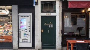 Un negozio con una porta verde, una macchina distributrice e un tavolo con sedie all'esterno.