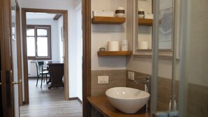 Un bagno moderno con un ampio lavandino bianco, mensole in legno e una porta doccia in vetro.