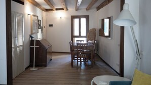 Un corridoio che conduce a una sala da pranzo con pavimento in legno, un tavolo con sedie e una lampada bianca.