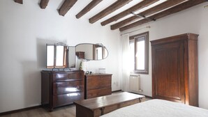 Una camera da letto con un letto di legno, una cassettiera con specchio, un termosifone e un armadio in legno.