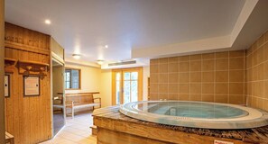 Ein Wellnessbereich mit Whirlpool, Holzliegen und einer gefliesten Wand.