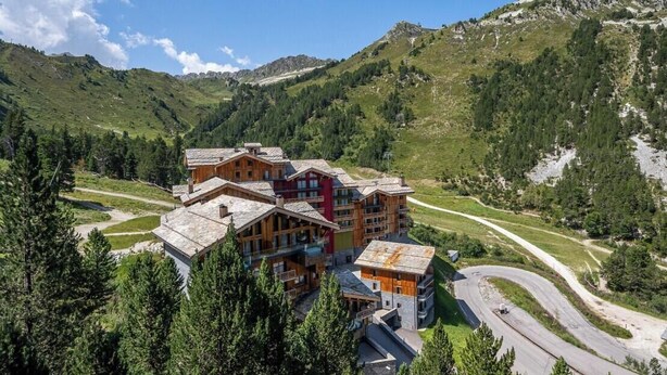 Un refugio de montaña con varias construcciones de madera, rodeado de exuberante vegetación y un camino sinuoso.