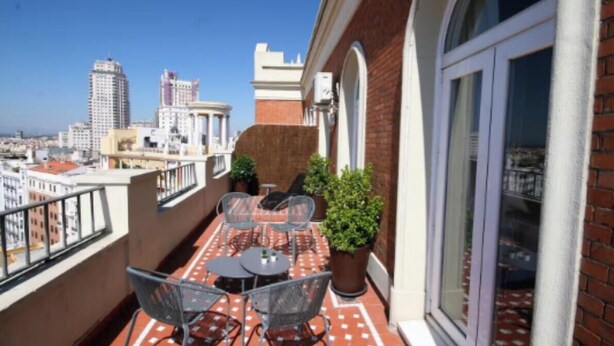 En balkon med et bord, stole, plantekasser og udsigt over byen.