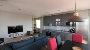 En moderne stue med sofa, spisebord og et køkkenområde med skabe og hårde hvidevarer.