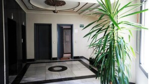 Et hotel lobby med flisegulv, to døre, en stor potteplante og en ventilator i loftet.