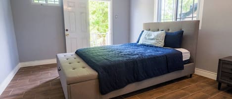 A bedroom with a bed, a bench, a window, and a door.