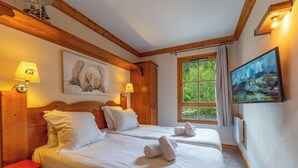 Habitación de hotel con dos camas, cabeceros de madera, un cuadro en la pared, una ventana con cortinas y un televisor.
