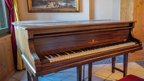 Un piano de cola con acabado de madera y el logotipo de Steinberg, ubicado en una habitación con piso de baldosas y un cuadro enmarcado en la pared.