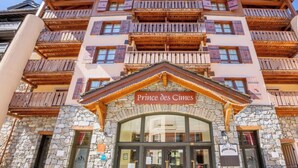 Entrada de un hotel con fachada de piedra, balcones de madera y un cartel que dice 'Prince des Cimes'.
