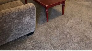 Una sala de estar con un sofá marrón, una mesa de centro de madera, un televisor sobre un mueble de madera y una puerta que da a otra habitación.
