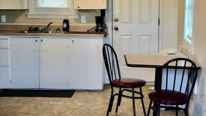 Cocina con armarios blancos, una ventana, un fregadero y un comedor con dos sillas.