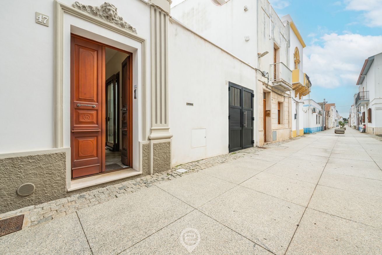 Uma rua estreita com um edifício branco, porta de madeira e portão preto.