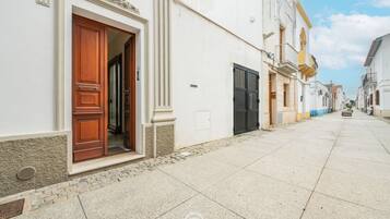Uma rua estreita com um edifício branco, porta de madeira e portão preto.