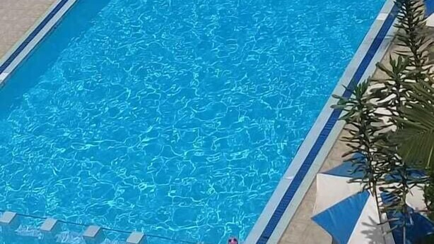 Een rechthoekig zwembad met helderblauw water, omringd door ligbedden en parasols.
