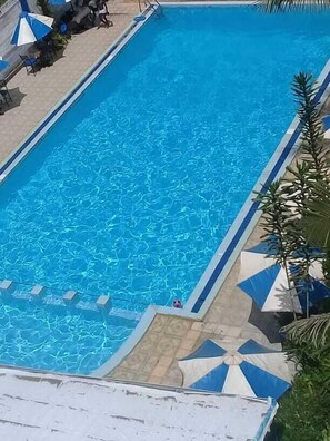 Une piscine rectangulaire à l’eau d’un bleu cristallin, entourée de chaises longues et de parasols.