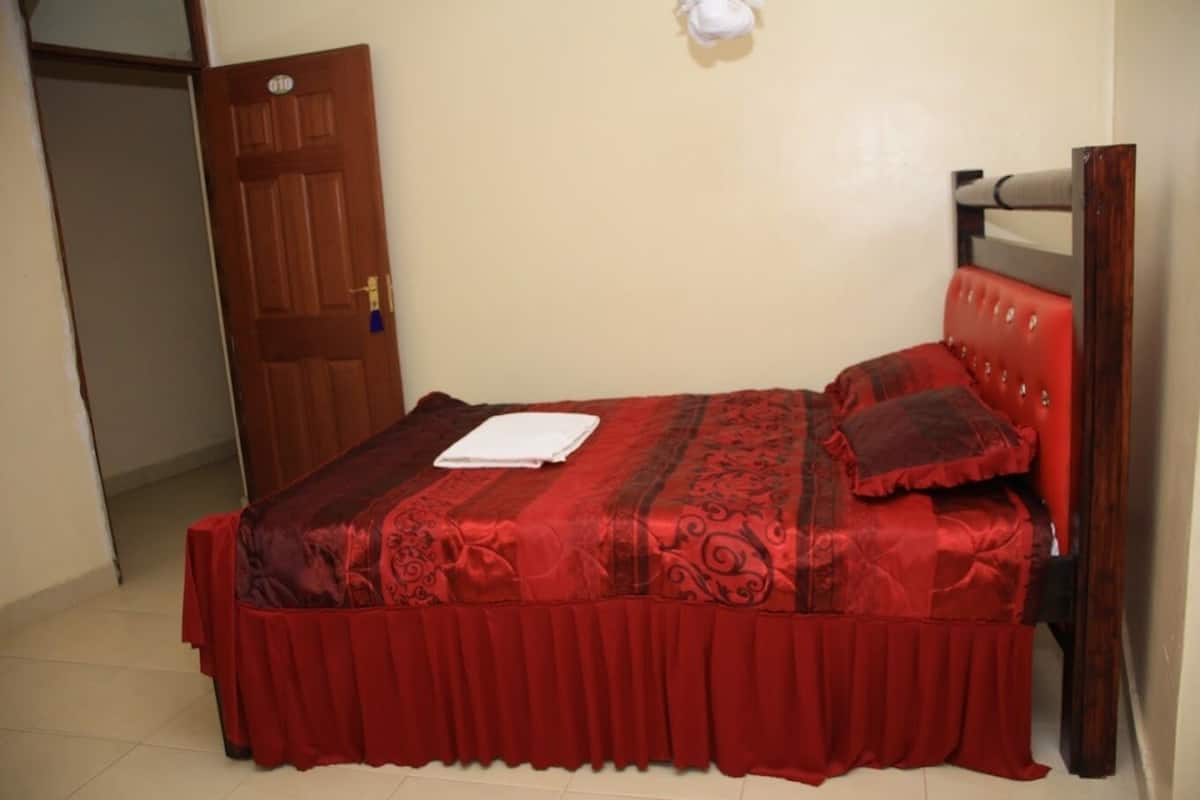 Ein Einzelbett mit roter Bettdecke und passenden Kissen, ein weißes Handtuch und ein hölzernes Kopfende.
