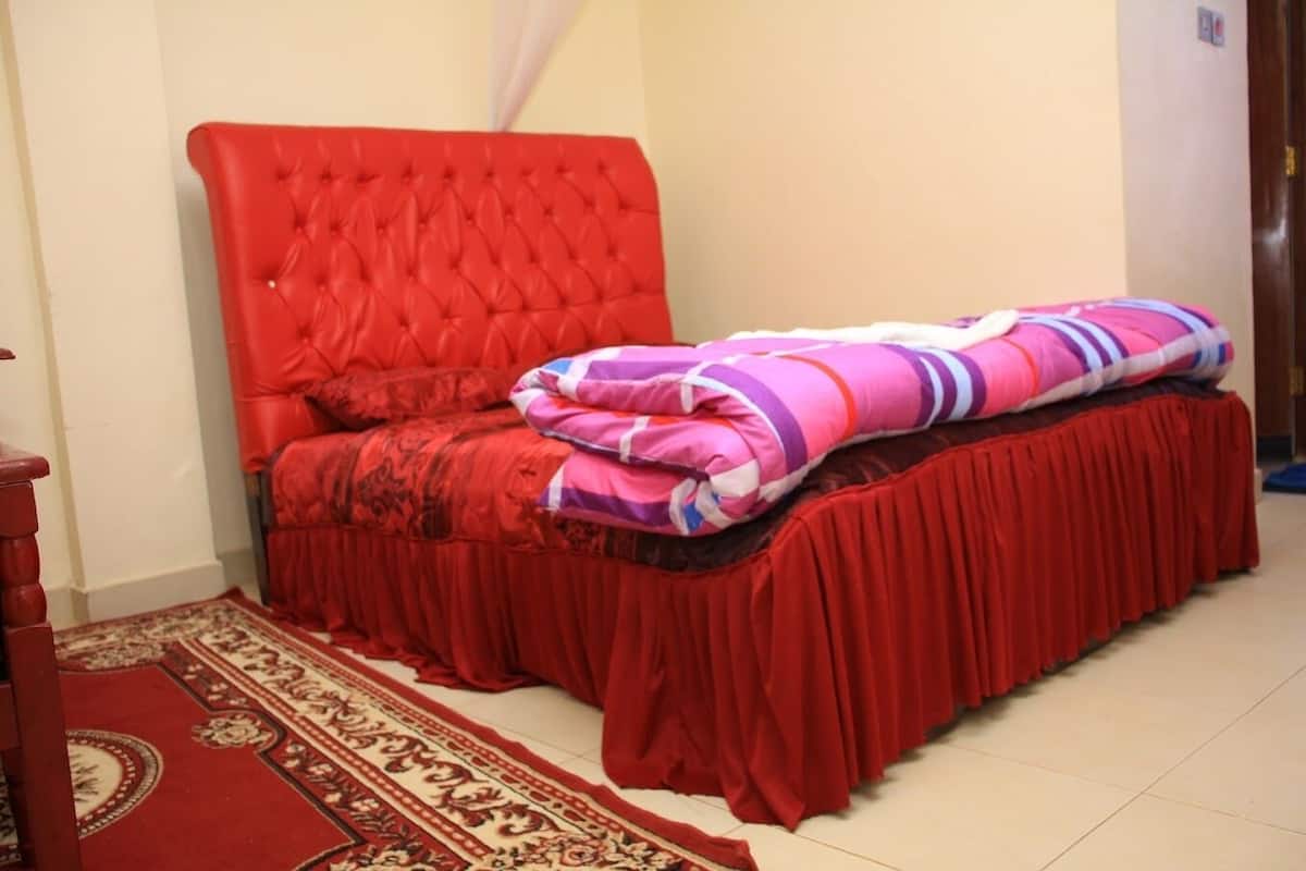 Ein Schlafzimmer mit einem roten, gepolsterten Bett, einem roten Bettvorhang und einem gemusterten Teppich.